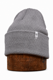 A gray ribbed knit beanie hat displayed on a brown wooden stand against a plain white background.