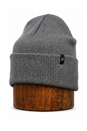 A gray ribbed knit beanie hat with a small black logo patch on the front cuff, displayed on a round wooden stand against a plain white background.