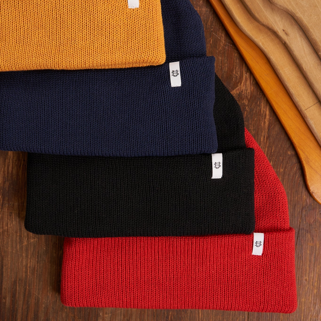 Stack of knit beanies in yellow, navy, black, and red on a wooden surface.