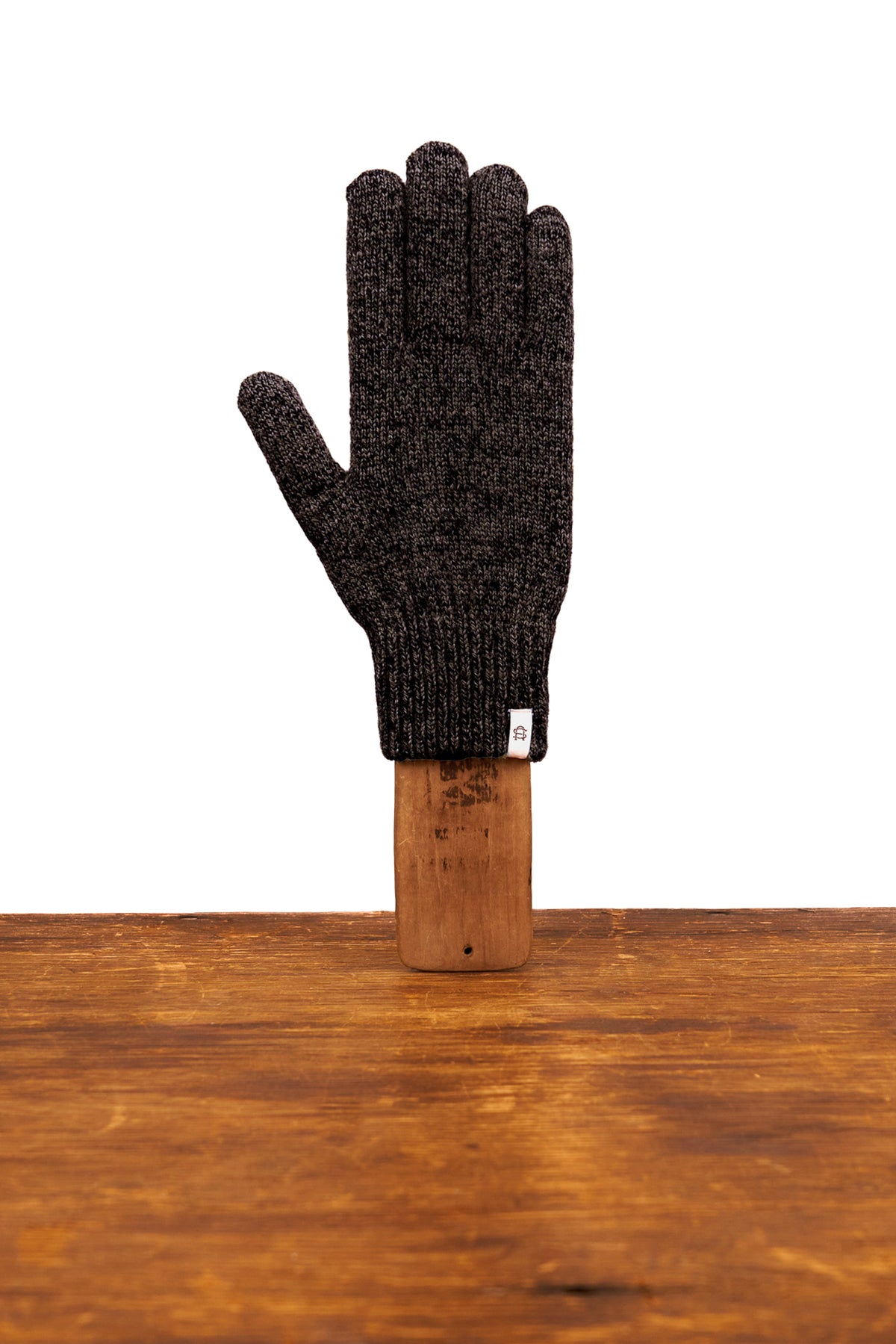 Black knitted glove on a wooden block against a white background
