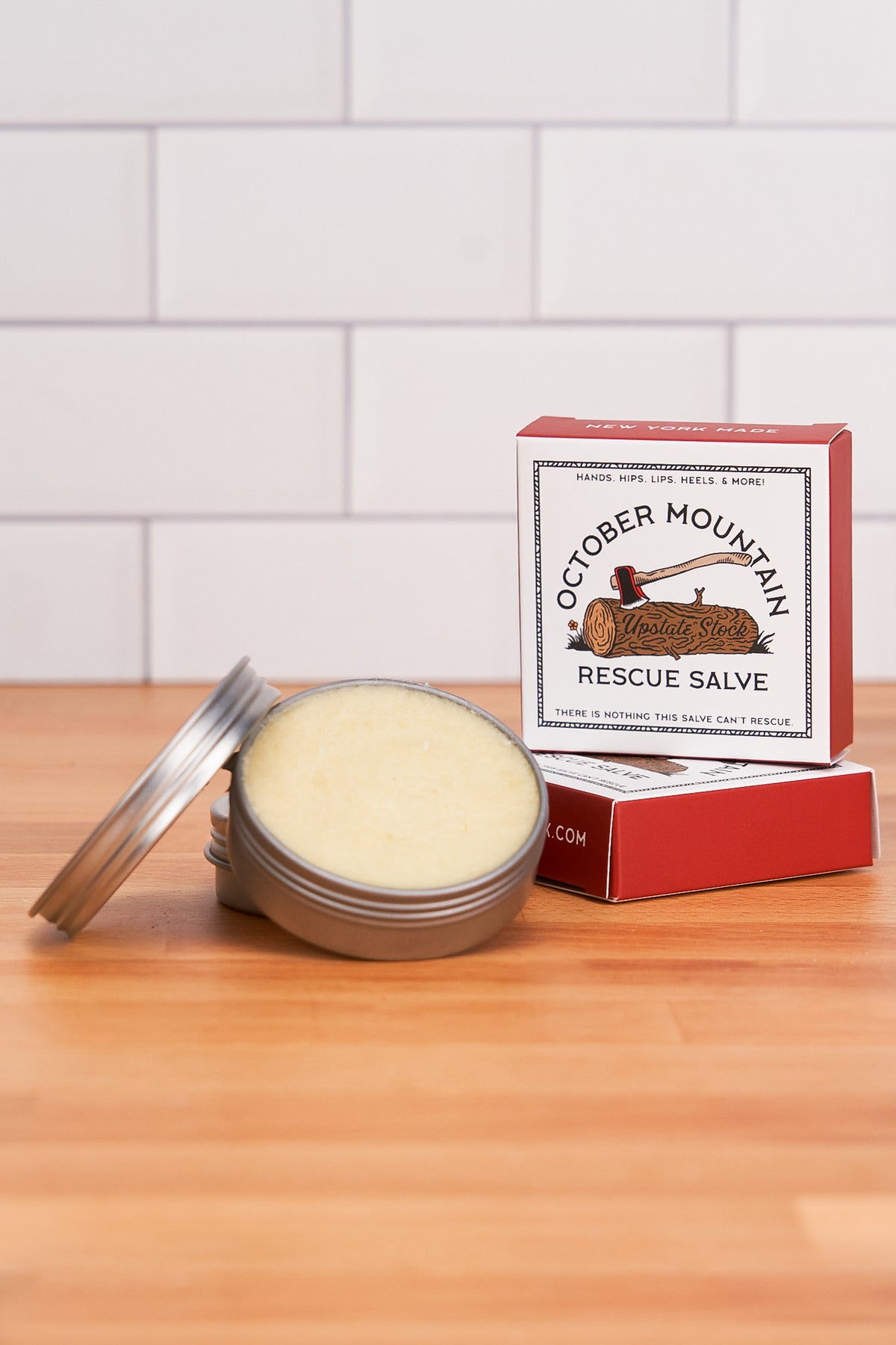 Open jar of October Mountain Rescue Salve on a wooden surface with the closed box in the background.