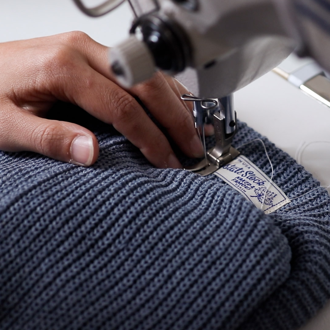 Person sewing blue fabric with a sewing machine, focusing on the stitching process.